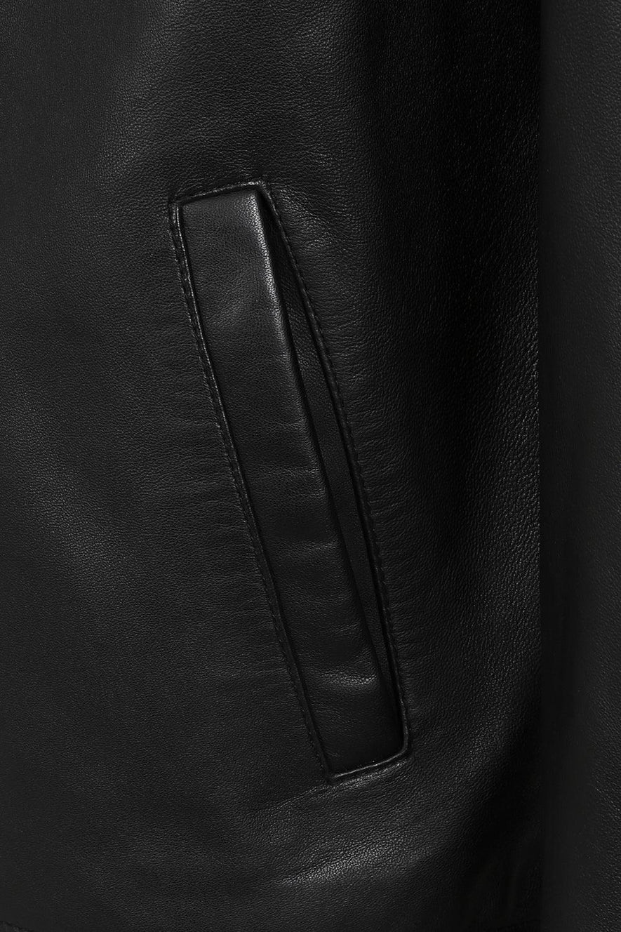 Close-up of a black leather jacket showing a vertical welt pocket with matching black leather trim and stitching.