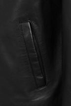Close-up of a black leather jacket showing a vertical welt pocket with matching black leather trim and stitching.