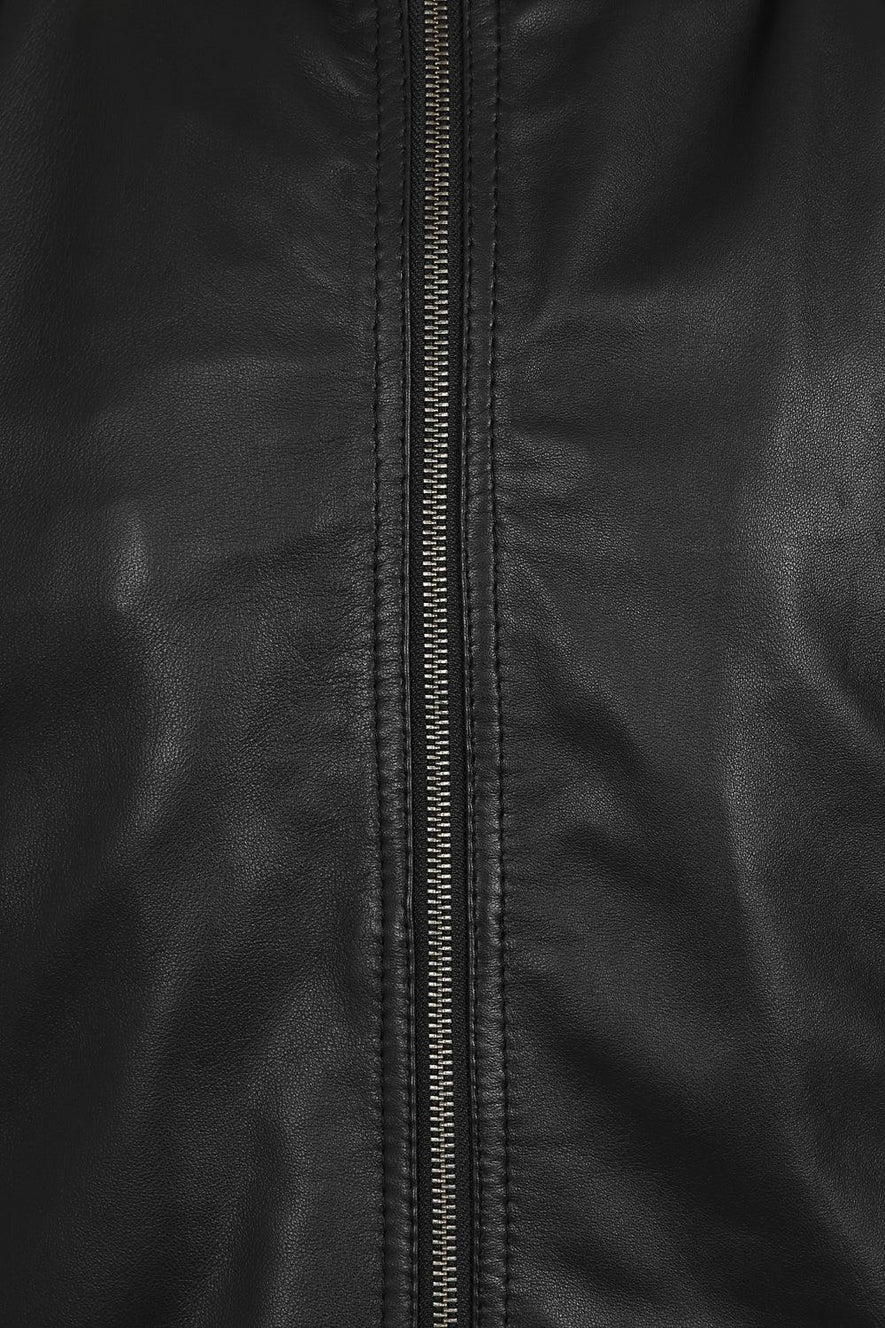 Close-up of a black leather jacket with a central metal zipper and visible stitching.