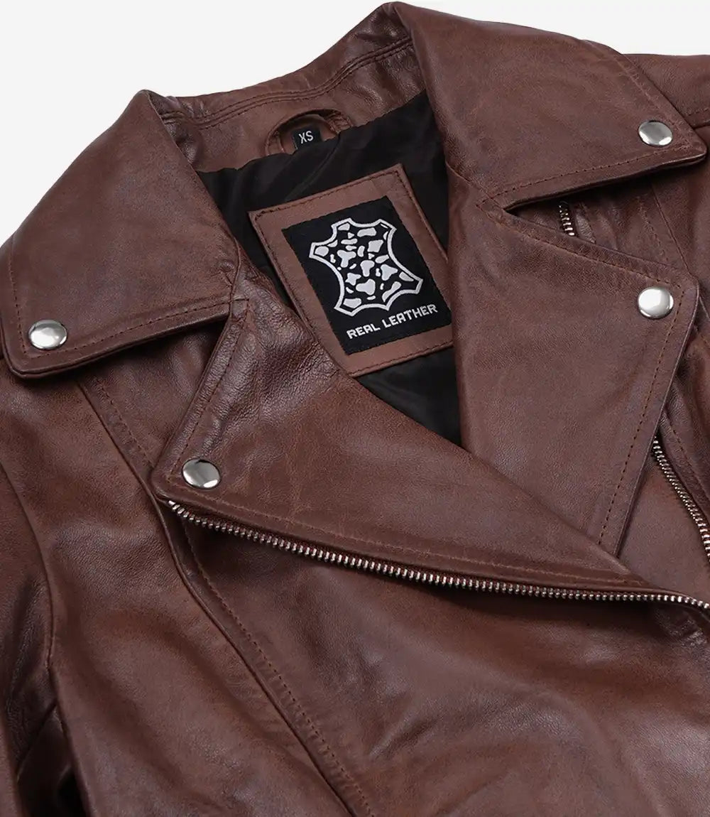 A close-up of a brown leather jacket showing the collar, snap-buttoned shoulder tabs, and an asymmetrical zipper. A black brand patch reading 'REAL LEATHER' is visible inside the collar.